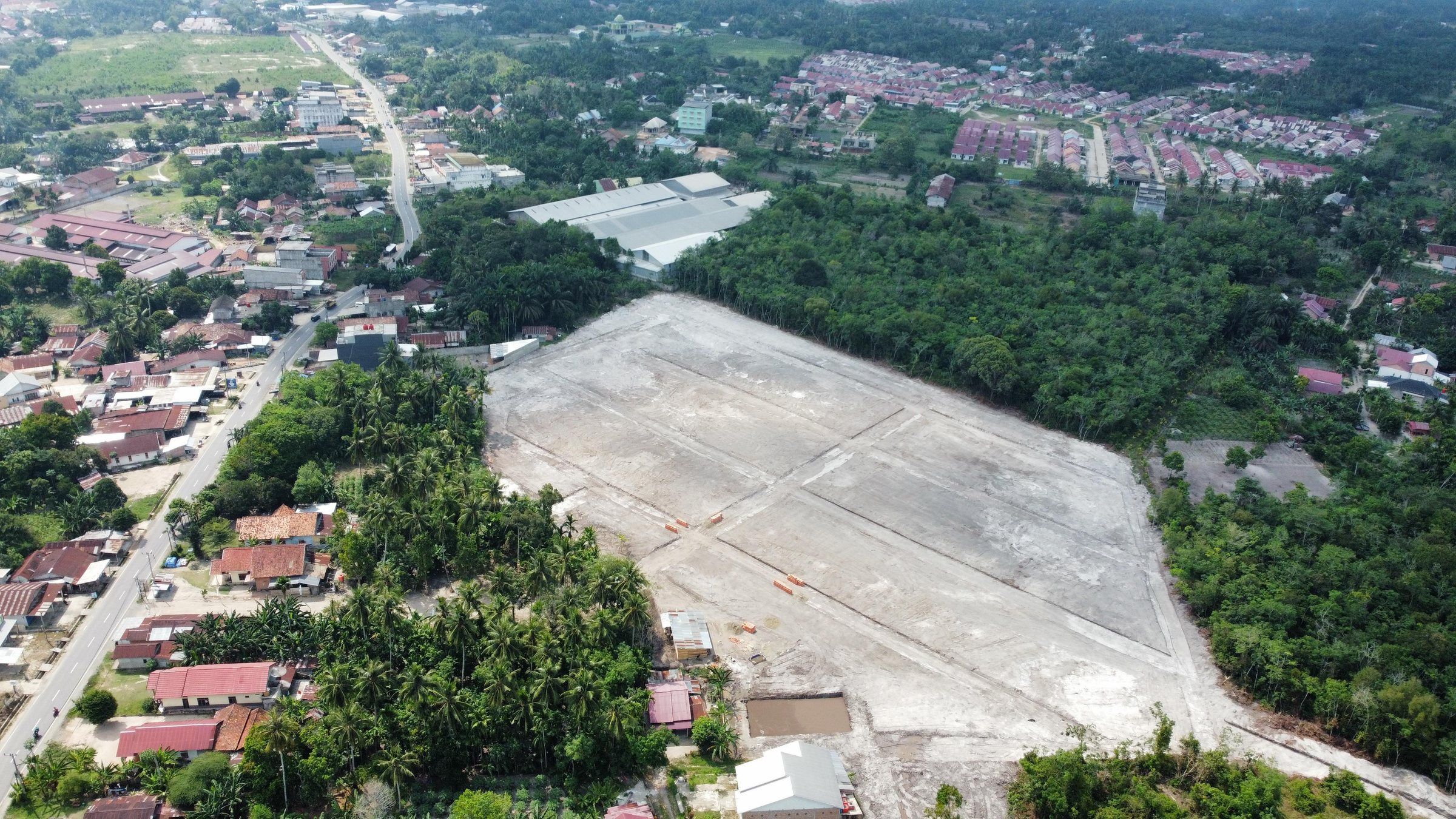Foto udara lahan luas yang sudah diratakan dan dibagi per petak, di tepi permukiman